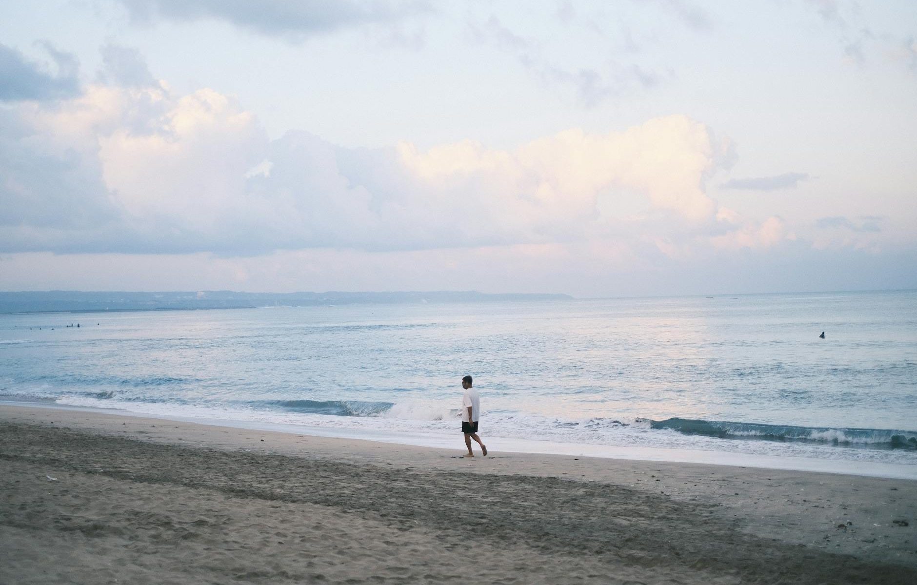 "Pemandangan indah sunset di pantai Kuta, Bali dengan ombak biru laut dan pasir putih halus."