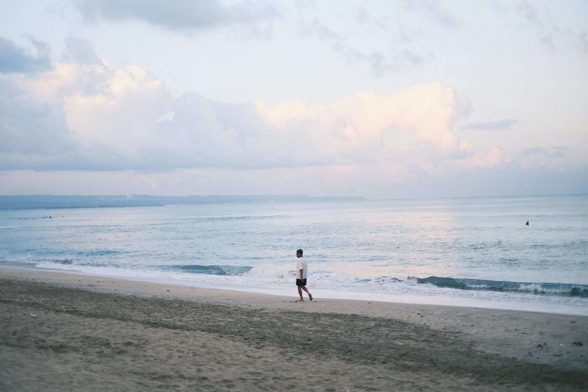 "Pemandangan indah sunset di pantai Kuta, Bali dengan ombak biru laut dan pasir putih halus."